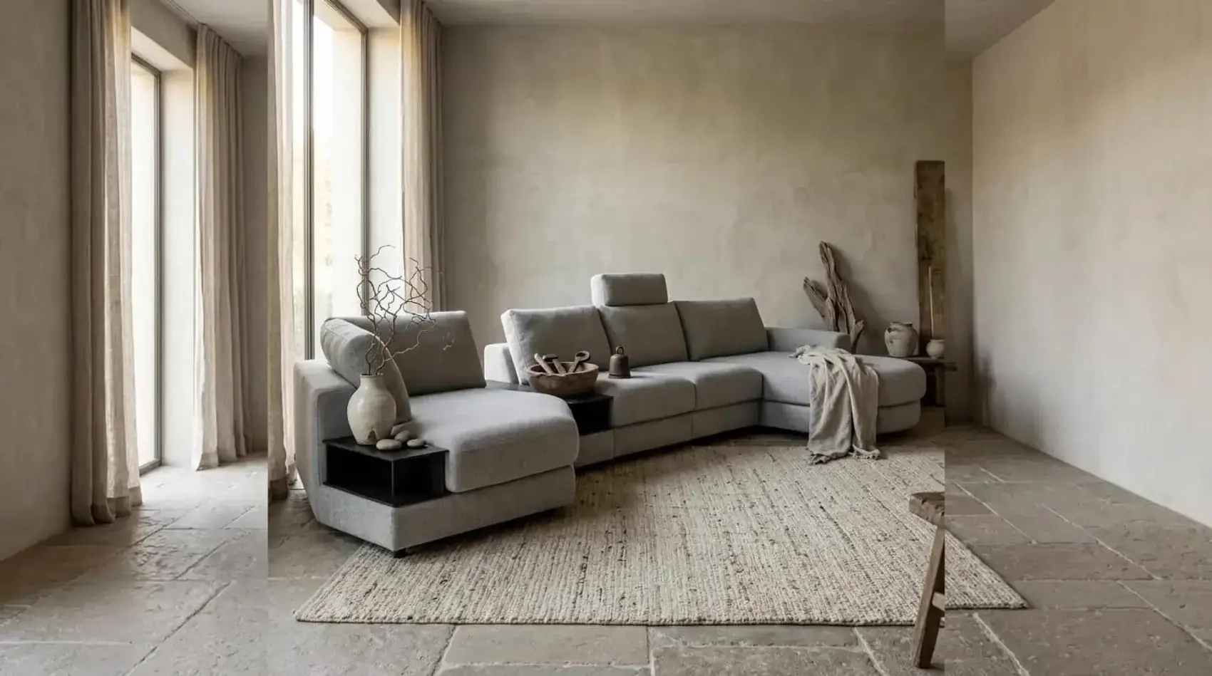 Grijze hoekbank Mirable met chaise longue en zwarte tussentafel voor een gepleisterde wand op een jute vloerkleed