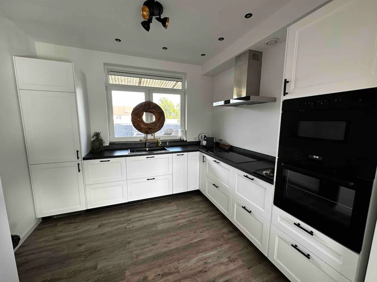 Moderne witte hoekkeuken met inductiekookplaat, vaatwasser, oven, magnetron en Nespresso