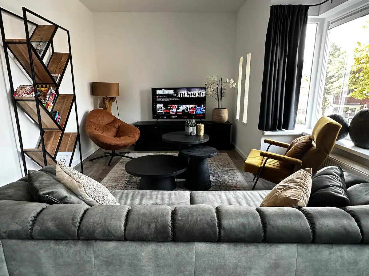 Zithoek met 55 inch smart-tv, cognac draaifauteuil, gele fauteuil en open boekenkast